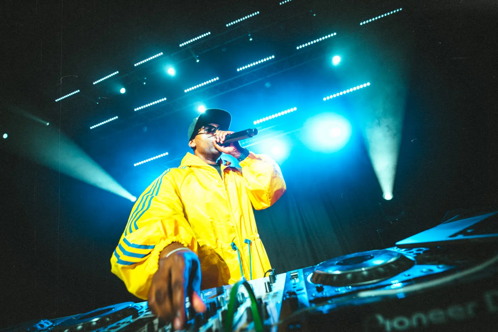 Hurrican X in a yellow jacket on stage under blue lights